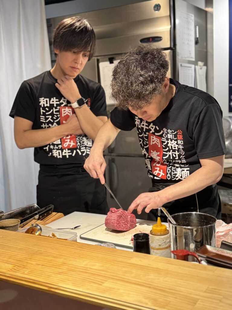 カウンターの中で赤身の塊に包丁を入れる料理長